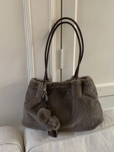 Sac seau en fausse fourrure marron avec double pompons sur un canapé blanc