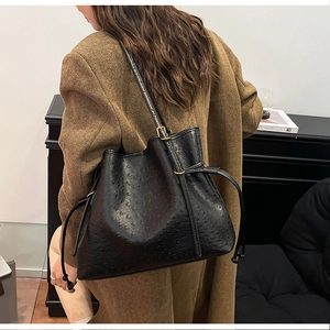 Detail of black ostrich embossed bucket bag with drawstring on a brown suit model