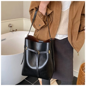 Detail of a minimalist black leather bucket bag with a wrap-around buckle and knotted strap