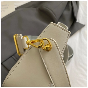 Detail view of smooth off-white leather shoulder bag with polished gold metal twist lock