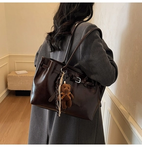 Detail of glossy dark brown tote bag with bear charm and striped strap on model