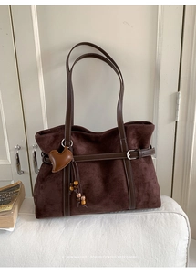 Detail of dark brown suede tote bag featuring leather straps and heart charm pendant