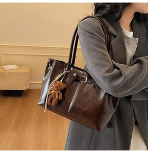 Detail of dark brown glossy leather tote bag with a cute bear charm on a female model