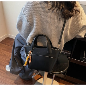 Detail of a black bucket bag with a colorful beaded charm and adjustable strap for women