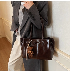 Detail of a large dark brown leather tote bag with buckle straps and a teddy bear charm