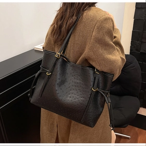 Detail of black ostrich-embossed shoulder bag with golden hardware on a wool coat