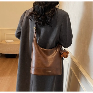 Detail of soft vintage leather shoulder bag with wide strap and plush bear charm decoration