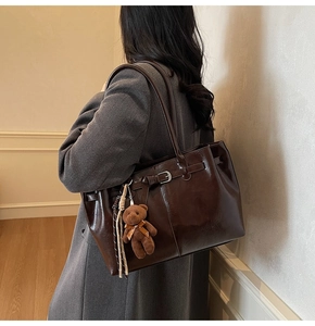 Detail of dark brown glossy tote bag with teddy bear charm and braided tassel detail