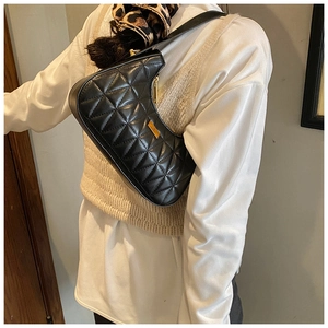 Detailed view of black quilted crescent shoulder bag with golden hardware on a model