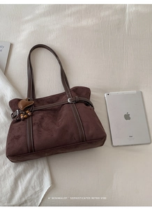 Detail of dark brown suede tote bag with leather straps and heart charm on white bedding