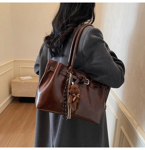 Brown oil-wax leather tote bag detail with plush bear charm and side buckle strap