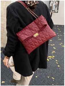 Detail of burgundy quilted chain bag featuring gold twist lock on autumn street background