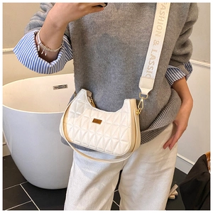 Close-up of quilted white crescent bag with gold hardware and wide fashion strap