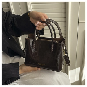 Détail du sac à main marron foncé texture crocodile avec garniture dorée et logo