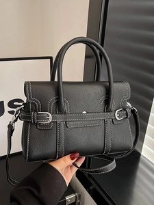 Black leather handbag with white stitching and silver buckle in professional setting