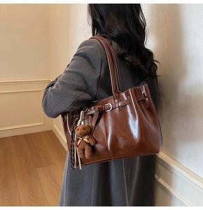 Detail of dark brown glossy leather tote bag featuring a cute plush bear charm