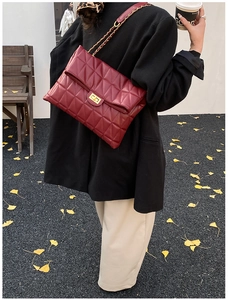 Detail of wine red quilted leather shoulder bag with golden chain strap on autumn street