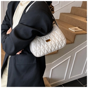 Close-up of white quilted underarm bag with gold metal buckle worn on the shoulder