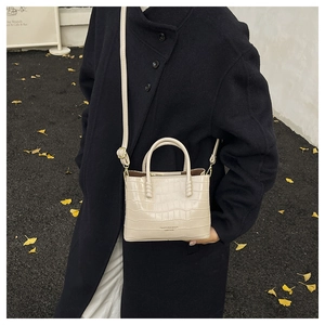 Détail d'un sac à main beige gaufré crocodile porté sur un manteau d'hiver noir élégant