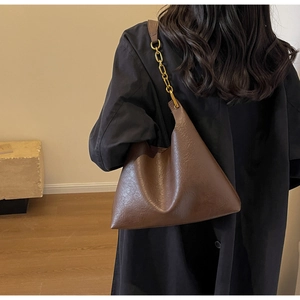 Détail du sac bandoulière en cuir marron foncé avec texture vintage et chaîne dorée