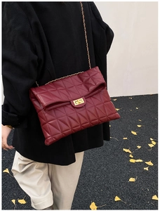 Close-up of burgundy quilted chain bag with gold twist lock on autumn ginkgo background
