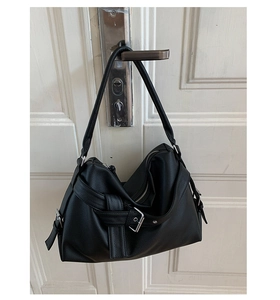 Close-up of black lychee texture tote bag with metal buckle hanging on a door handle