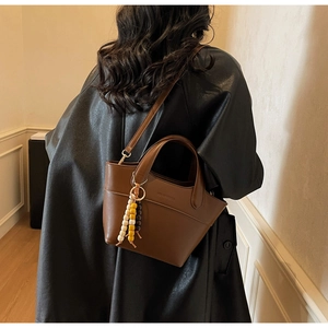 Detail view of a brown leather bucket bag with colorful bead charm and long shoulder strap