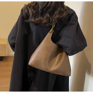 Gros plan sur un sac hobo en cuir marron souple porté avec un manteau sombre, style vintage