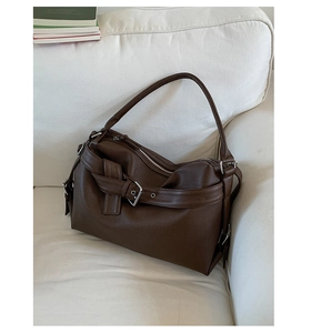 Detail of dark brown pebble leather tote bag with silver buckle on a white sofa