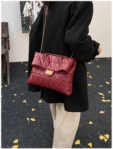 Detail of burgundy quilted chain bag with gold twist lock worn outdoors by a model