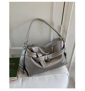 Detailed view of silver faux leather tote with textured finish and buckle on white sofa