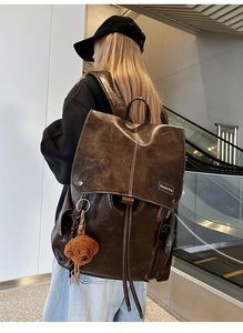 Detailed side view of large vintage dark brown leather backpack with teddy bear charm