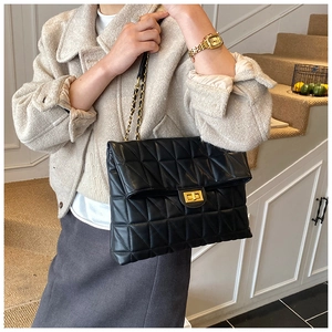 Close-up of black quilted leather shoulder bag with golden chain strap on a model