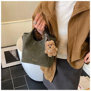 Detail of dark green bucket bag with gold lettering and cute brown plush bear charm