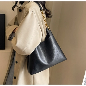 Détail d'un grand sac cabas noir en cuir avec des anses élégantes en chaîne dorée