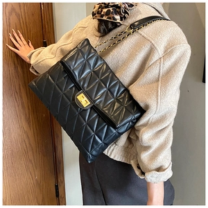 Close-up of black quilted leather bag with gold chain strap worn by a model in a beige coat
