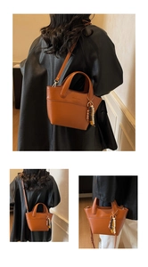 Detail of brown leather bucket bag featuring debossed logo and beaded charm accessory