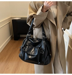 Detail of a large black leather tote bag with silver buckles and a front flap pocket