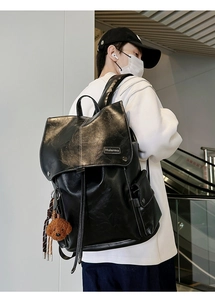 Close-up of black leather backpack with flap pockets and a small teddy bear charm