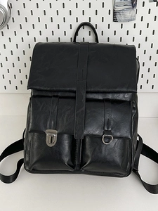 Front view of a black faux leather backpack with silver buckles on white pegboard background