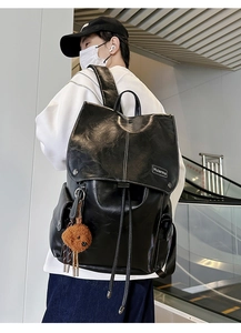 Close-up of vintage black leather backpack featuring flap cover and cute bear charm