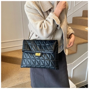 Detail of black quilted chain bag with gold rotating lock on model shoulder