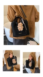 Detail of a black suede bucket bag featuring a brown teddy bear charm and gold lettering
