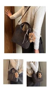 Detail of dark charcoal bucket bag with gold logo, curved handle and plush bear charm