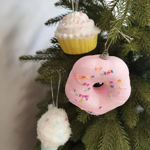Détail d'ornements de beignet et cupcake pailletés suspendus à une branche de sapin de Noël