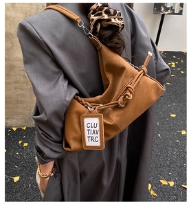 Détail d'un sac hobo en daim marron avec sangle nouée porté sur un blazer gris foncé