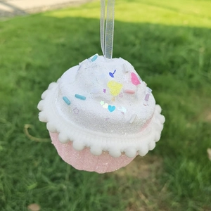 Pendentif cupcake rose avec glaçage blanc et paillettes sur un fond de pelouse verte