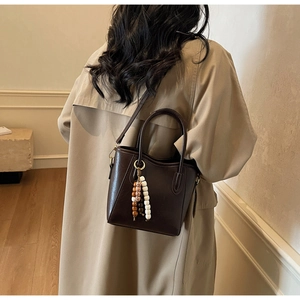 Détail du sac seau en cuir marron foncé avec pompon en perles de bois sur manteau