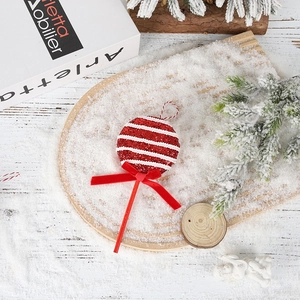 Detail of red and white candy cane ornament with glitter and bow on a snowy tray