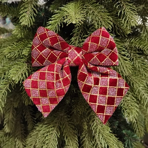 Red velvet Christmas bow with gold glitter grid pattern on festive pine tree branch